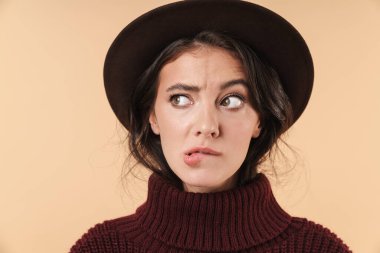 Gergin, esmer bir kadının bej duvar arkasında yalnız poz verirken çekilmiş bir fotoğrafı..