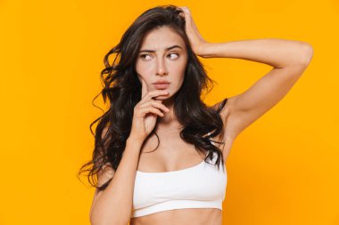 Mayo giymiş kafası karışmış genç bir kadının görüntüsü. Sarı duvarın ötesine izole edilmiş bir şekilde düşünüyor ve bakıyor.