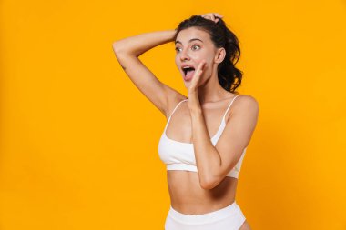 Güzel, heyecanlı, mayo giymiş, sarı duvarda izole bir şekilde bağırıp çağıran bir kadın resmi.