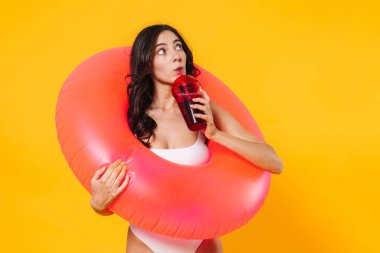 Lastik halkalı, yukarı bakan ve sarı duvardan izole edilmiş gazoz içen bir kadın.