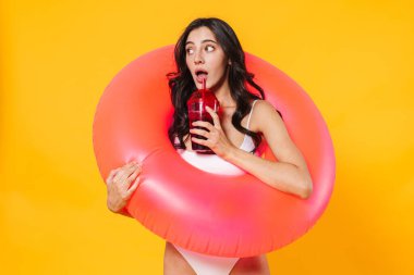 Şaşırmış kauçuk yüzüklü bir kadının görüntüsü. Sarı duvardan izole edilmiş soda içiyor.