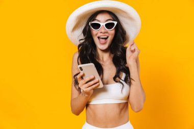 Mayolu ve şapkalı bir kadının sarı duvarda izole bir şekilde cep telefonu kullanması.