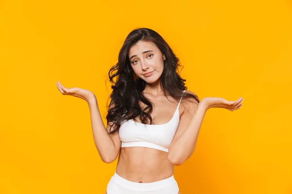 Image of young confused woman in swimsuit holding copyspace and looking at camera isolated over yellow wall