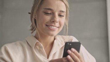 Evde kanepede otururken akıllı telefon kullanan çekici bir kadın.