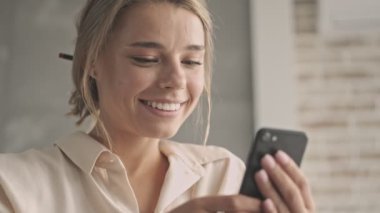 Evdeki kanepede otururken akıllı telefon kullanan çekici sarışın kadın.
