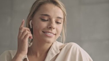 Kulaklıklı, çekici, sarışın bir kadın evde telefonla konuşuyor.