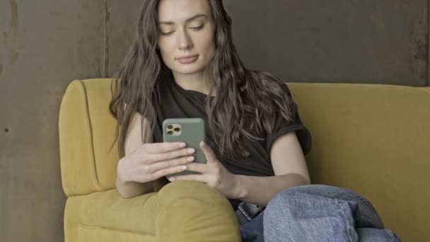 Klidný Hezká Brunetka Žena Pomocí Smartphone Zatímco Sedí Pohovce Uvnitř — Stock video