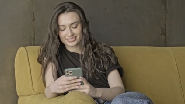 Mulher Bonita Morena Agradável Usando Smartphone Enquanto Sentado Sofá Dentro — Vídeo de Stock