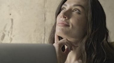 Mutlu, düşünceli, güzel, esmer bir kadın laptopuyla evde kanepede otururken bir şey düşünüyor.