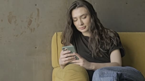 Mulher Morena Bonita Concentrada Usando Smartphone Enquanto Sentada Sofá Dentro — Vídeo de Stock