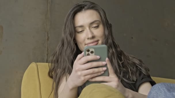 Ευτυχισμένη Όμορφη Μελαχρινή Γυναίκα Χρησιμοποιώντας Smartphone Ενώ Κάθεται Εσωτερικό Καναπέ — Αρχείο Βίντεο