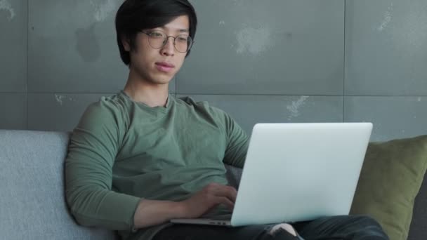 Atractivo Joven Asiático Con Gafas Está Usando Portátil Mientras Piensa — Vídeo de stock