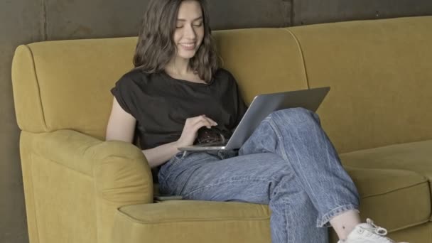 愉快的 沉思的 漂亮的黑发女人 她用手提电脑 坐在室内沙发上望着别处 — 图库视频影像
