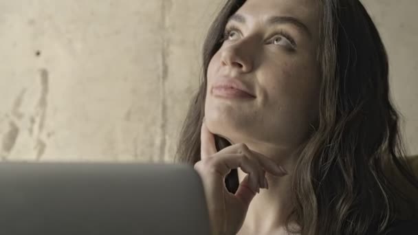 快乐的 沉思的 漂亮的黑发女人坐在家里的沙发上 一边想着什么 一边带着笔记本电脑 — 图库视频影像