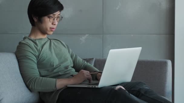 Vážný Mladý Asijský Muž Nosí Brýle Pracuje Svým Notebookem Sedí — Stock video