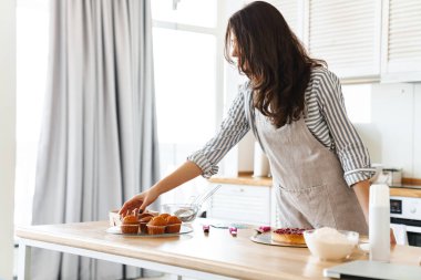 Modern mutfakta üzerinde yemek tarifi olan önlük giymiş esmer bir kadın resmi.