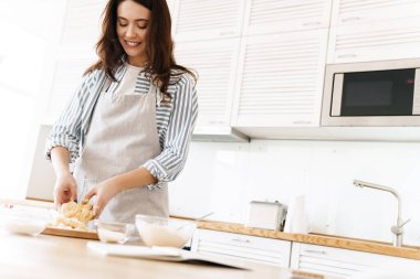 Modern mutfakta hamur yoğurmak için önlük giymiş beyaz bir kadın resmi.