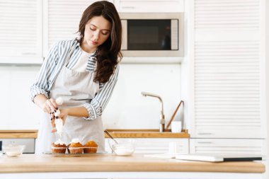 Kafkasyalı esmer kadının modern mutfakta kremalı kek pişirdiği görüntüsü.