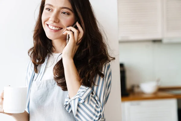 Изображение Счастливой Красивой Женщины Фартуке Разговаривающей Мобильному Телефону Пьющей Кофе — стоковое фото