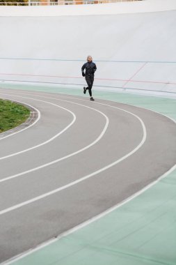 Stadyumdaki yarış pistinde koşan kendinden emin genç sporcu.