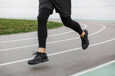 Açık stadyumdaki yarış pistinde koşan genç formda sporcunun bacakları.