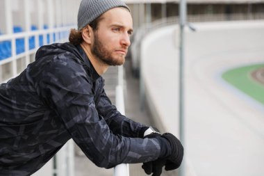 Çekici genç formda sporcu stadyumda antrenmandan sonra dinleniyor, demiryoluna yaslanıyor.