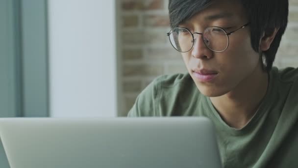 一位心平气和的年轻亚洲自由职业者戴着眼镜 坐在家里的桌子旁 用笔记本电脑近距离观察他的近照 — 图库视频影像