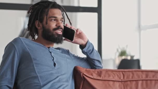 一位面带微笑 积极向上的非洲裔美国年轻人正在家里客厅里用智能手机交谈 — 图库视频影像