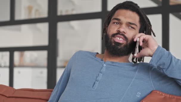 アフリカ系アメリカ人の若者が自宅のリビングルームでスマートフォンで話しています — ストック動画