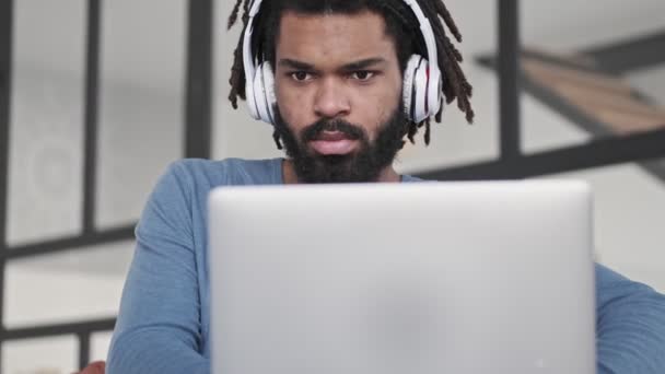 Skupiony Młody Afroamerykanin Słuchawkach Używa Swojego Srebrnego Laptopa Salonie — Wideo stockowe