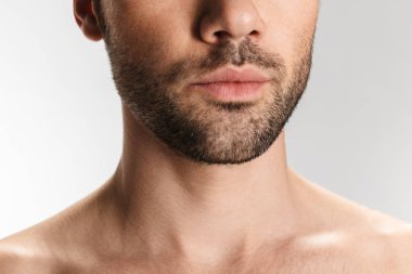 Tıraşsız, yarı çıplak bir adamın beyaz arka planda yalnız poz verirken çekilmiş bir fotoğrafı.