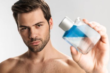 Beyaz arka planda izole edilmiş, poz veren ve parfüm gösteren yarı çıplak yakışıklı bir adamın fotoğrafı.