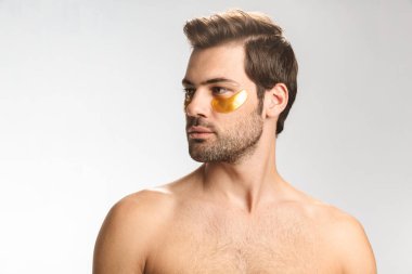 Ciddi yarı çıplak bir adamın fotoğrafı. Göz bantlı, poz veren ve beyaz arka planda izole edilmiş bir şekilde duran.