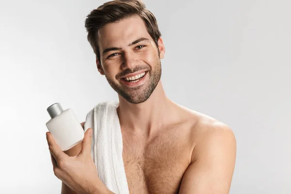 照片上 一个快乐的半裸男子拿着毛巾摆姿势 在白色的背景上展示了保湿乳液 — 图库照片