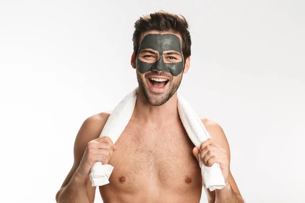 照片中快乐的半裸男子 脸上戴着化妆品黏土面具 毛巾被白色背景隔开笑着 — 图库照片