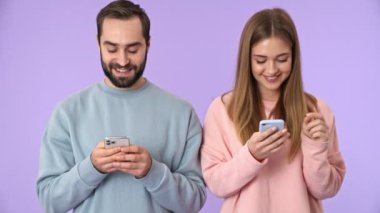 Gülümseyen genç çift mor arka planda akıllı telefon kullanıyor.