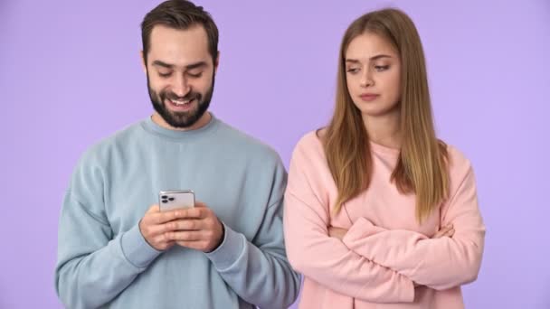 笑顔Beaded男使用スマートフォン中に彼女のDisplied可愛いですブロンドガールフレンド上の紫の背景 — ストック動画