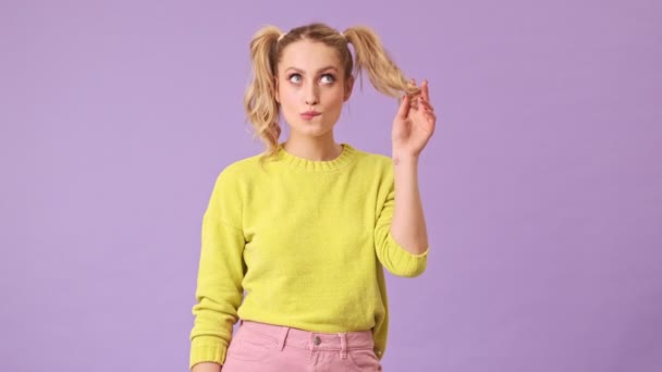 스웨터를 금발의 소녀가 시선을 돌리며 만지고 가리지 보라색 배경의 스튜디오에서 — 비디오