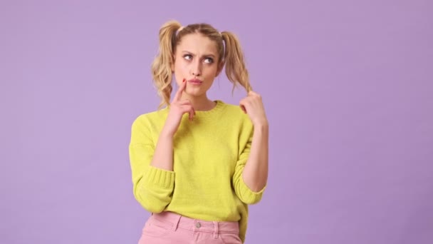一位无以伦比的金发姑娘若有所思地把头发放在她的手指上 在一个紫色背景的孤立的工作室里 把她的食指贴在她的脸颊上 — 图库视频影像