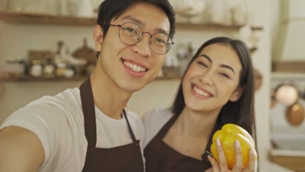 居心地の良いキッチンで時間を調理しながら面白い陽気なアジアのカップルの男と女が自撮り写真を撮っています — ストック動画