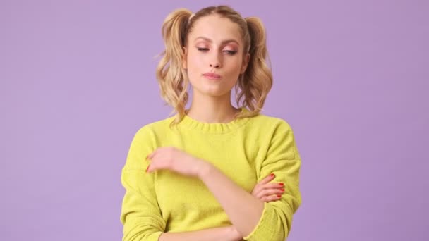 一个穿着黄色毛衣的漂亮姑娘在考虑求婚时 用一个伸出的手指捂住她的脸 但她不同意他的说法 摇着头 在一个紫色背景的与世隔绝的工作室里耸了耸肩 — 图库视频影像