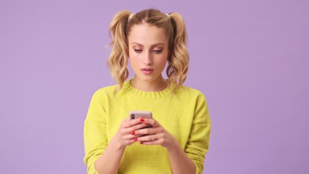 一位可爱的金发女郎正在电话上打字 并在一个紫色背景的孤零零的工作室里为对方的回答而高兴 — 图库视频影像