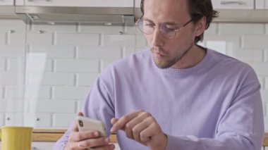 Gözlüklü yakışıklı adam evde kahvaltı ederken akıllı telefon kullanıyor.