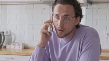 Gözlüklü yakışıklı adam evde masanın yanında akıllı telefonla konuşuyor.