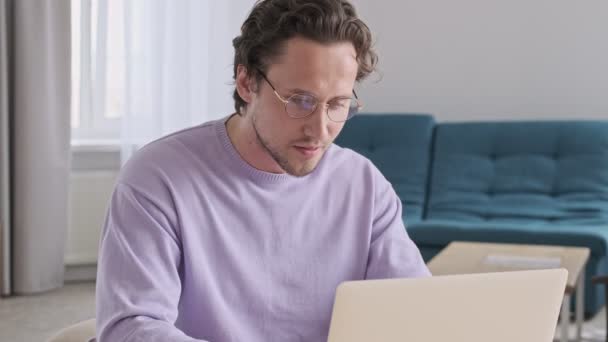 幸せなハンサムな男で眼鏡でラップトップコンピュータを使用してテーブルによって自宅 — ストック動画