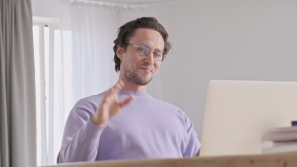 陽気なハンサムな男で眼鏡でビデオコールによってラップトップコンピュータ上で座っている間にテーブルに家 — ストック動画