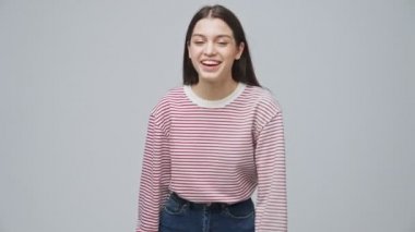 Neşeli, çekici esmer kadın. Gri arka planda el sallıyor ve eğleniyor.