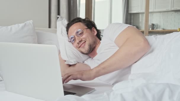 Hombre Guapo Feliz Gafas Usando Computadora Portátil Mientras Está Acostado — Vídeo de stock