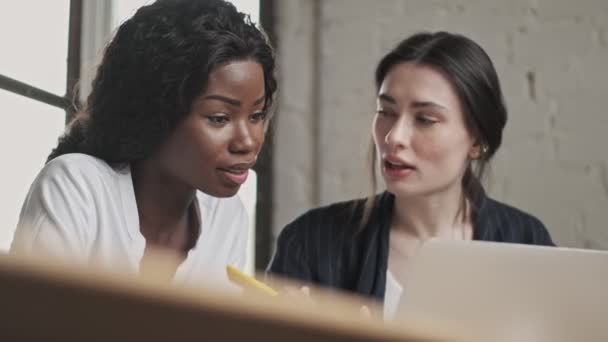 漂亮的跨国年轻黑发女商人同事一边在办公室用笔记本电脑一边讨论项目 — 图库视频影像