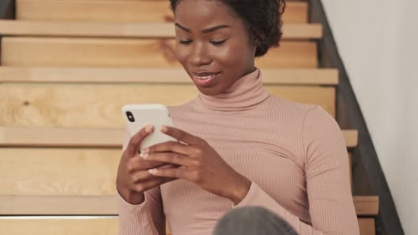 Una Joven Africana Sonriente Está Usando Teléfono Inteligente Mientras Está — Vídeo de stock